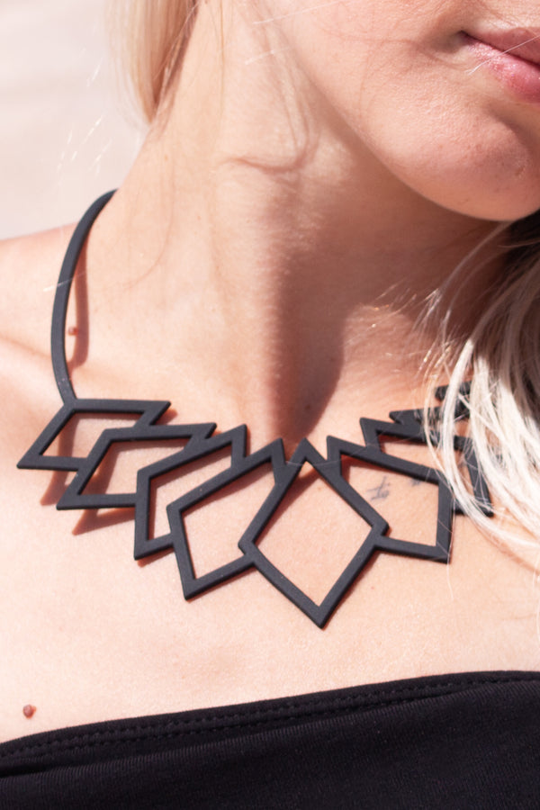 zoom, vue gros plan, collier diamant, couleur noir. Taille réelle. Bijoux fantaisies en silicone, ladygum, marque française, créateurs, designers. Style plastron, large, grand, graphique, géométrique, contemporain, triangle. Léger, souple, longueur réglable, ajustable, minimisant les allergies, résistant à l'eau, à la chaleur, fermoir en T. Cadeau original.