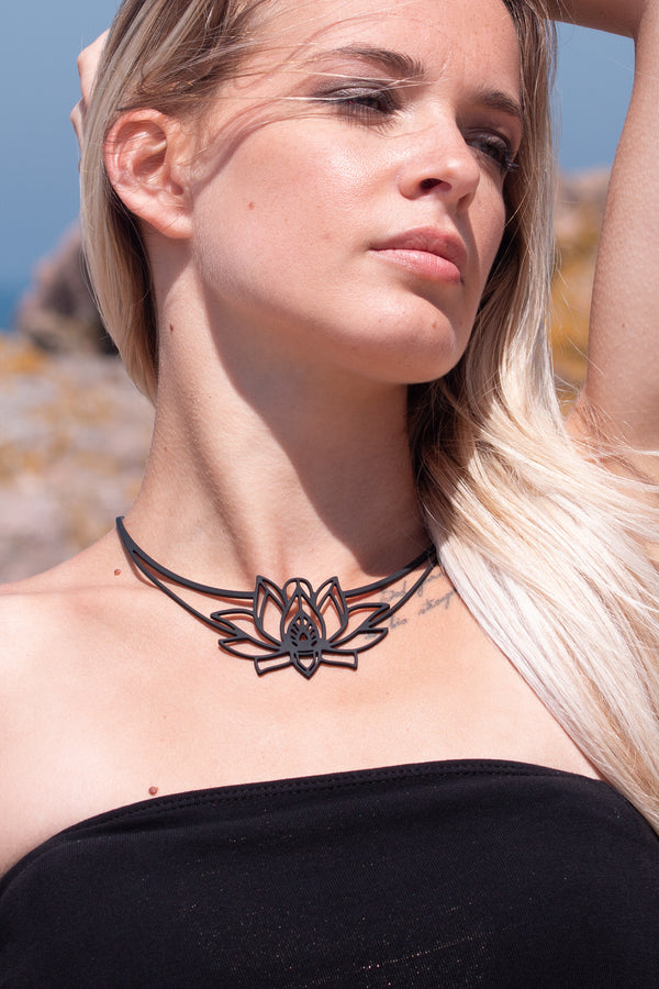 zoom, vue gros plan, collier mantra, couleur noir. Vue taille réelle, porté par mannequin dorine gaudin. Bijoux fantaisies en silicone, ladygum, marque française, créateurs, designers. Style plastron, fleur, nature, floral, lotus, nénuphar, zen, yoga, pétales, feuilles. Léger, souple, résistant à l'eau/à la chaleur/à la lumière. Collier ajustable, longueur réglable, fermoir en T. Cadeau original.