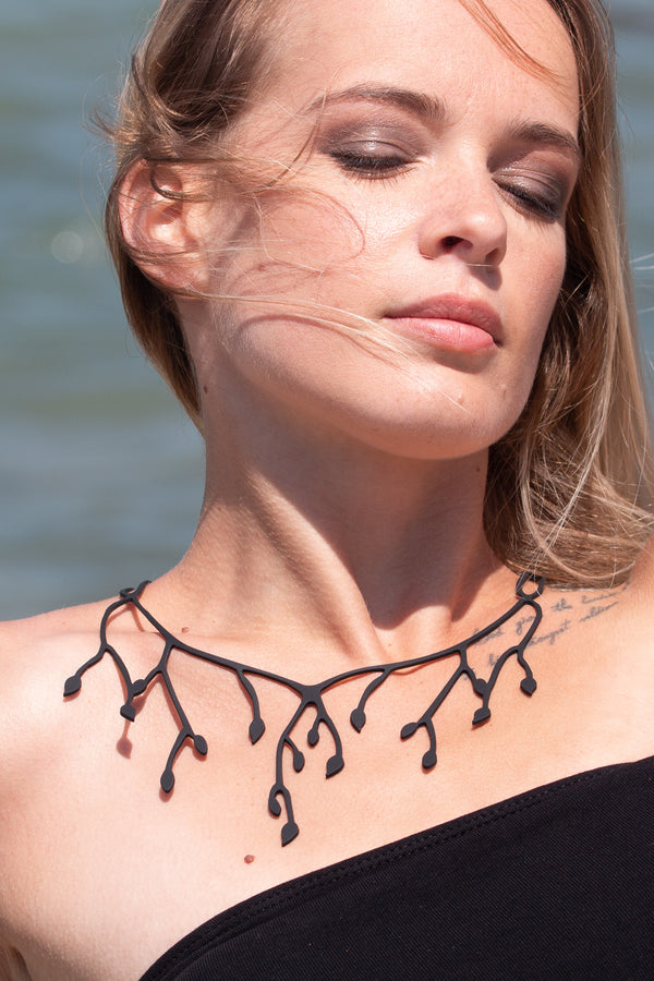 zoom, vue gros plan, collier primavera, couleur noir. Vue taille réelle, porté par mannequin dorine gaudin. Bijoux fantaisies en silicone, ladygum, marque française, créateurs, designers. Style long, pendant, plongeant, fleur, feuilles, nature, floral, pétales. Peut se porter à l'épaule. Léger, souple, résistant à l'eau/à la chaleur/à la lumière. Collier ajustable, longueur réglable, fermoir en T. Cadeau original.